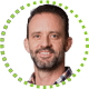 Portrait of a smiling man with short brown hair, beard, and mustache, wearing a plaid shirt. The image is framed by a circle of green dots on a white background.